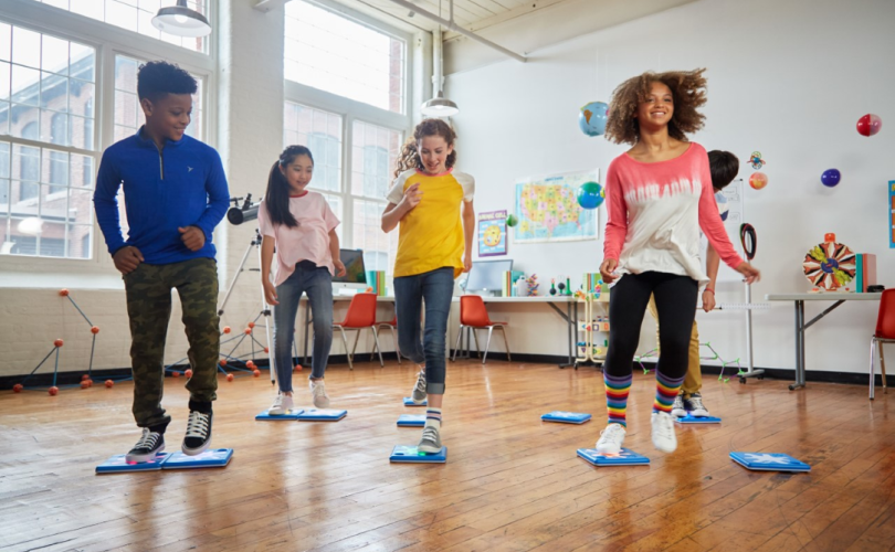 Four children in a classroom, jumping on programmable floor buttons