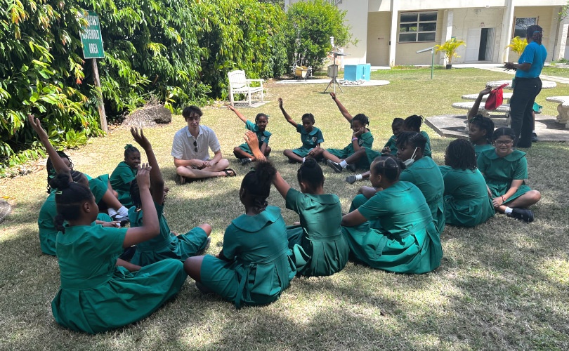 Elementary students sitting in a circle on the ground outside Bellairs