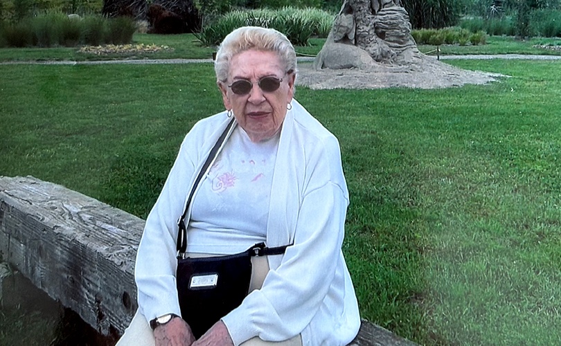 A woman sitting on a wooden bench in a park with green grass
