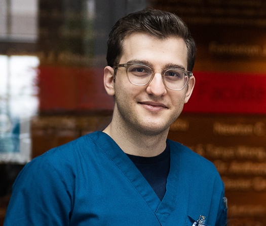A man smiling and wearing blue scrubs and glasses