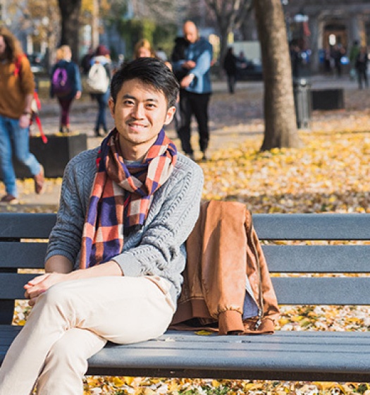 Lower campus in the autumn with student on bench with people walking on path nearby