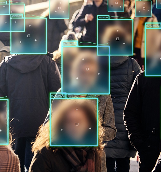 A crowded street scene with multiple people whose faces are obscured by digital blue squares and rectangles, simulating facial recognition or privacy masking technology. 