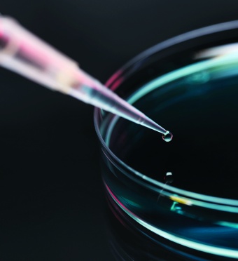 A pipette dropping a drop of liquid into a glass dish